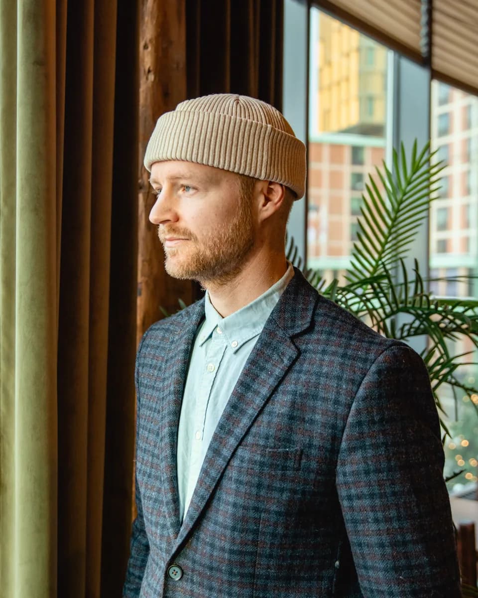 Jens Asp, fundador de MiradaDonante, con chaqueta de cuadros y gorro de punto beige, mirando por una ventana.